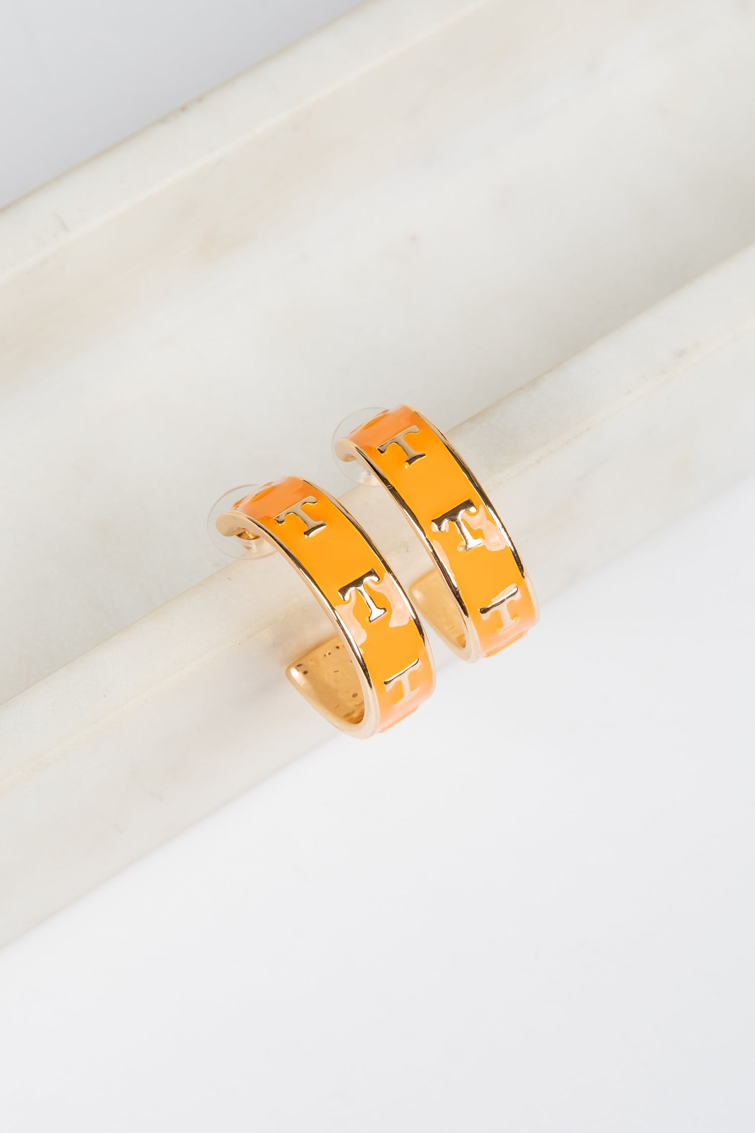 Pair of orange hoop earrings on a white surface