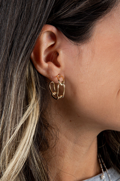 Close-up of a person wearing a gold hoop earring with hair and part of a denim shirt in the background.