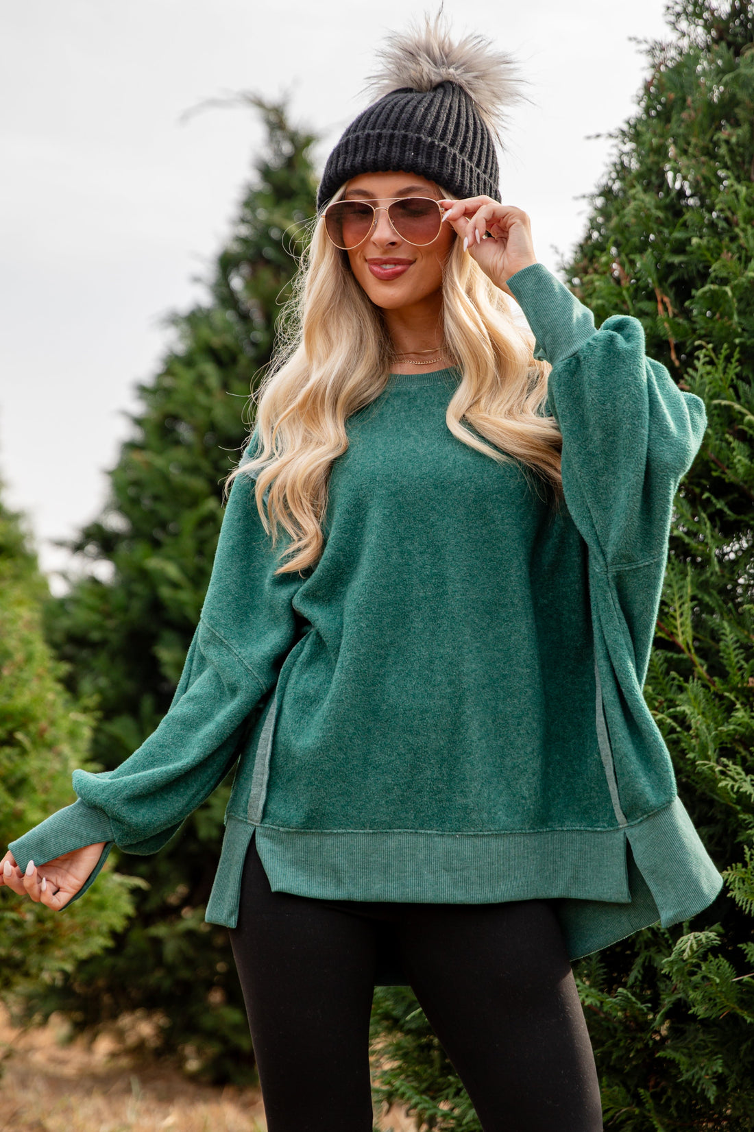 Woman wearing a teal sweater and black beanie outdoors with trees in the background