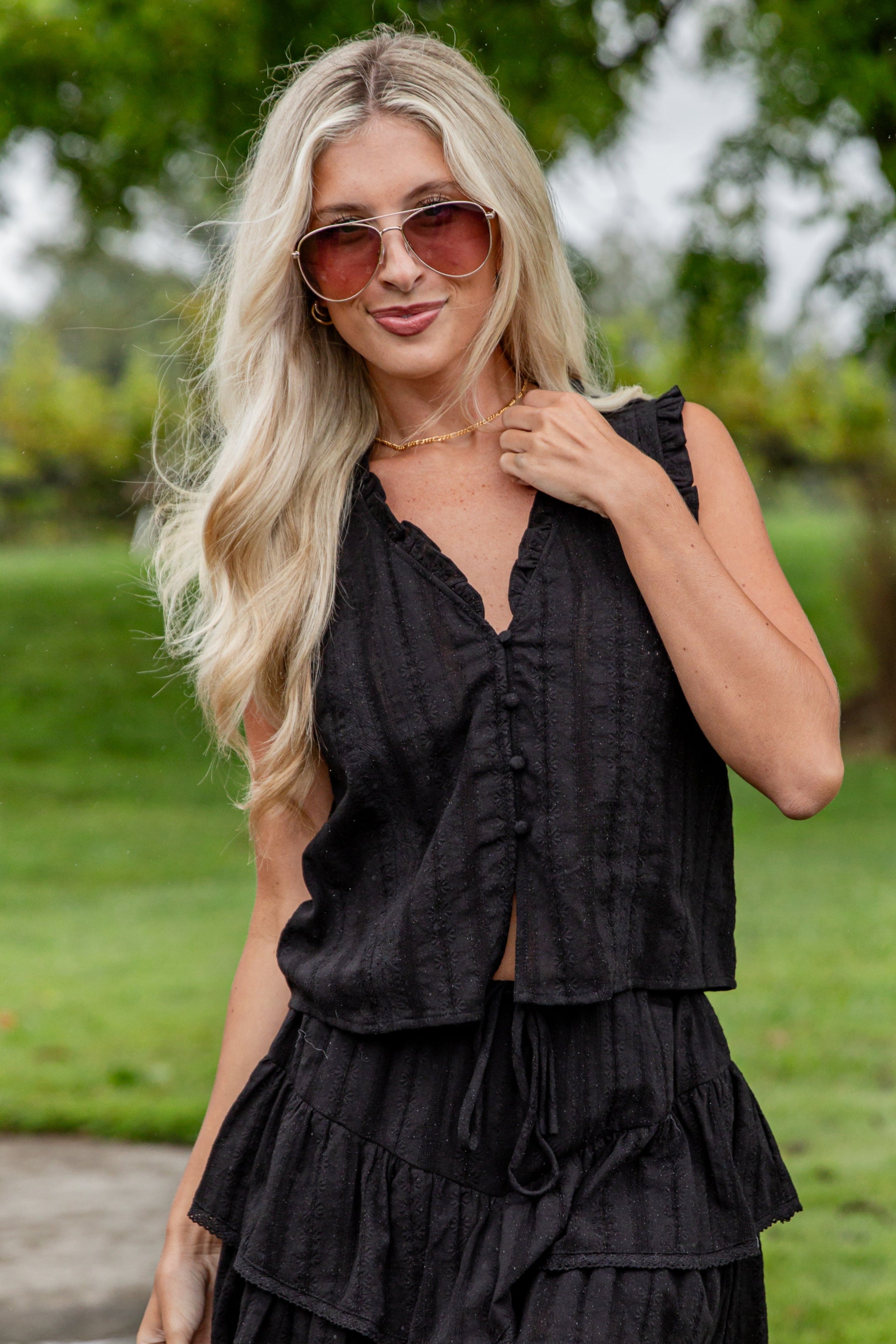 Woman wearing a black sleeveless dress with ruffles outdoors.