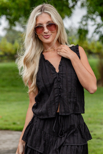 Woman wearing a black sleeveless dress with ruffles outdoors.