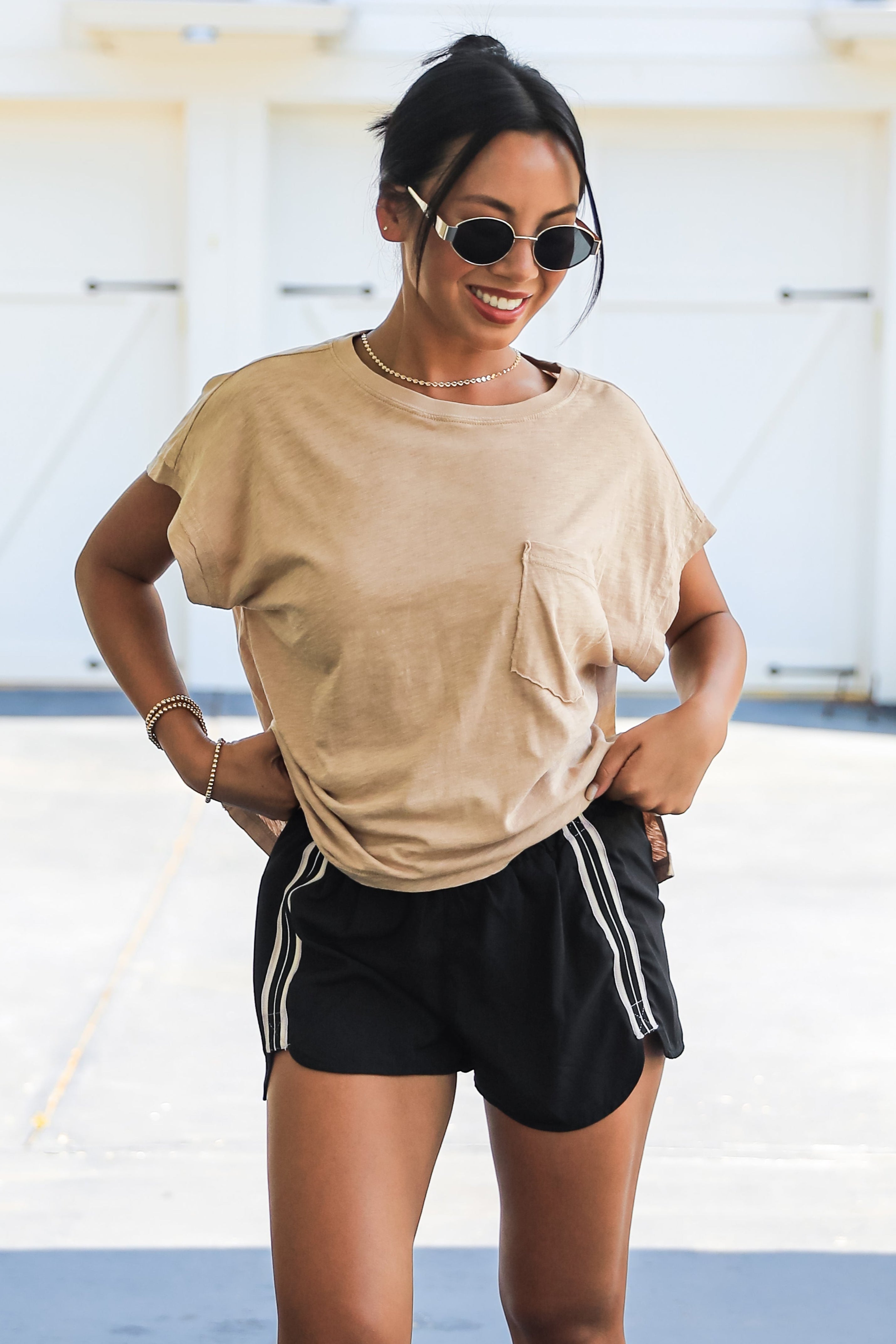 Woman wearing a beige t-shirt and black shorts with white stripes, standing indoors.
