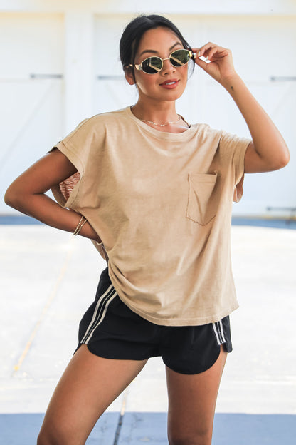Woman wearing a beige t-shirt and black shorts with white stripes outdoors.