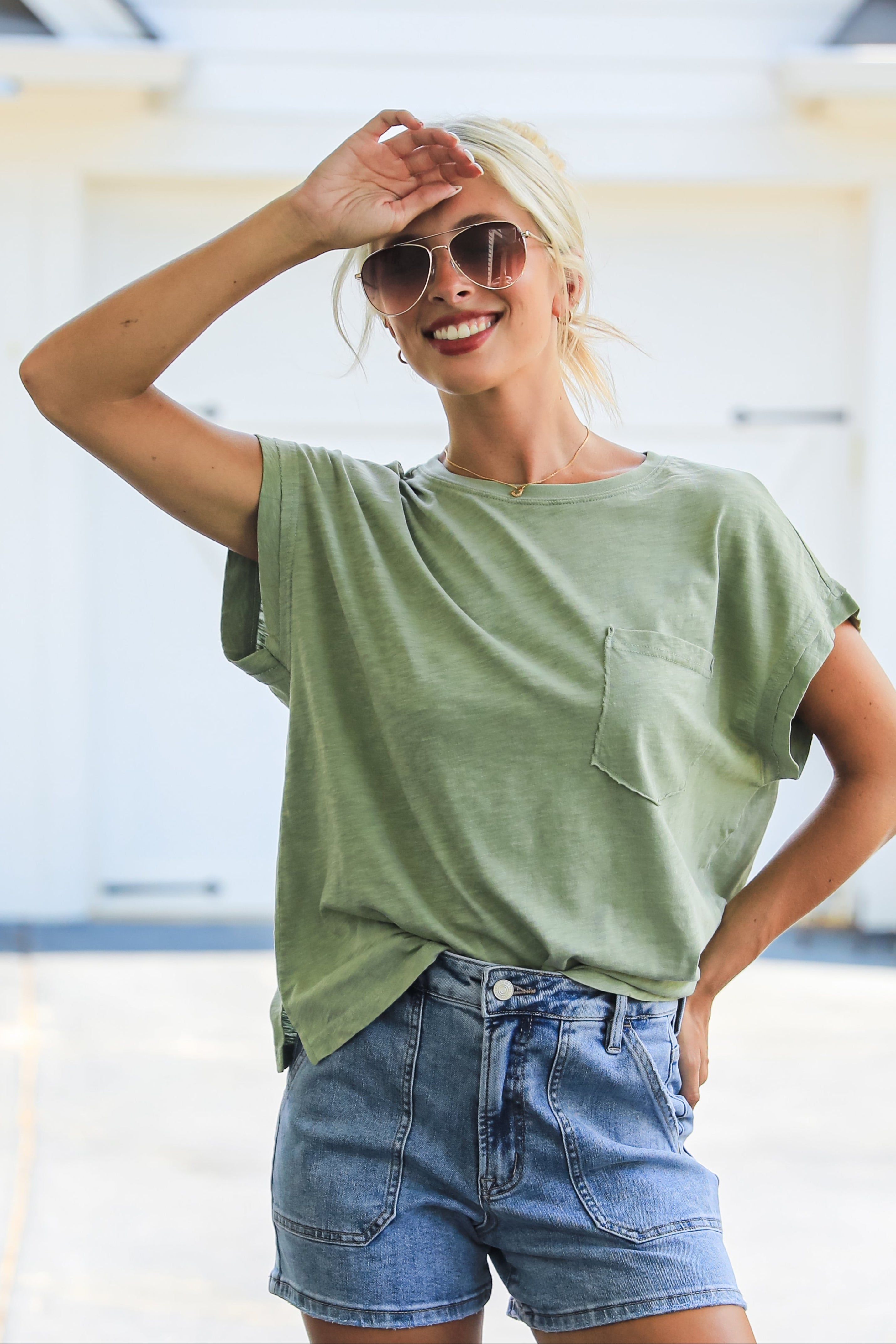 Woman wearing a green t-shirt and denim shorts, smiling outdoors.