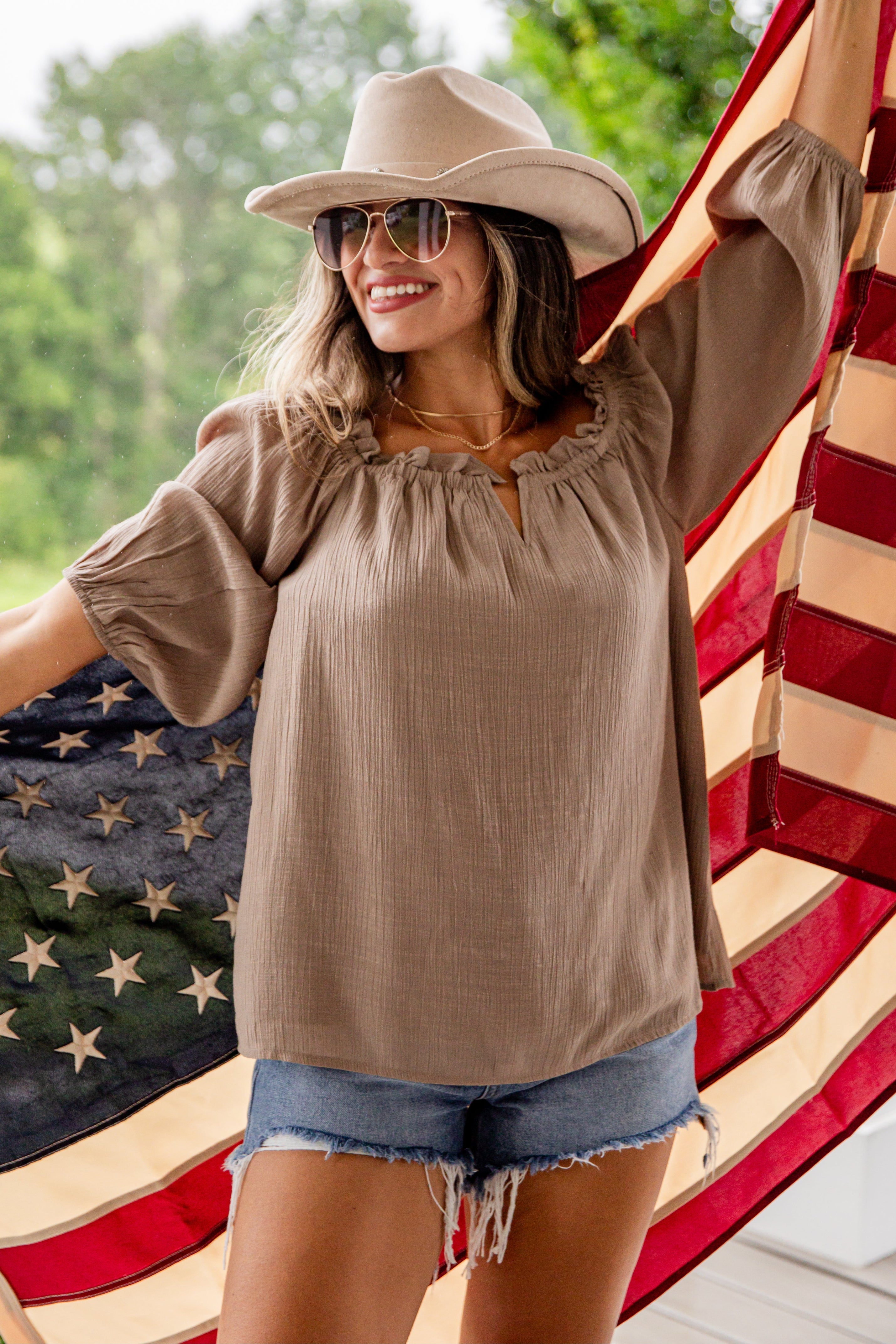Woman wearing a beige top and hat, standing in front of an American flag.