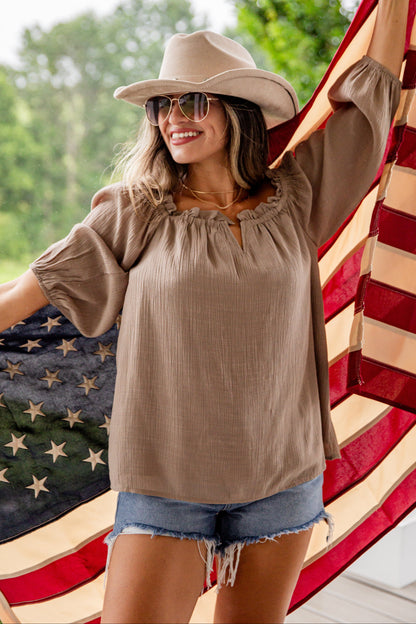 Woman wearing a beige top and hat, standing in front of an American flag.