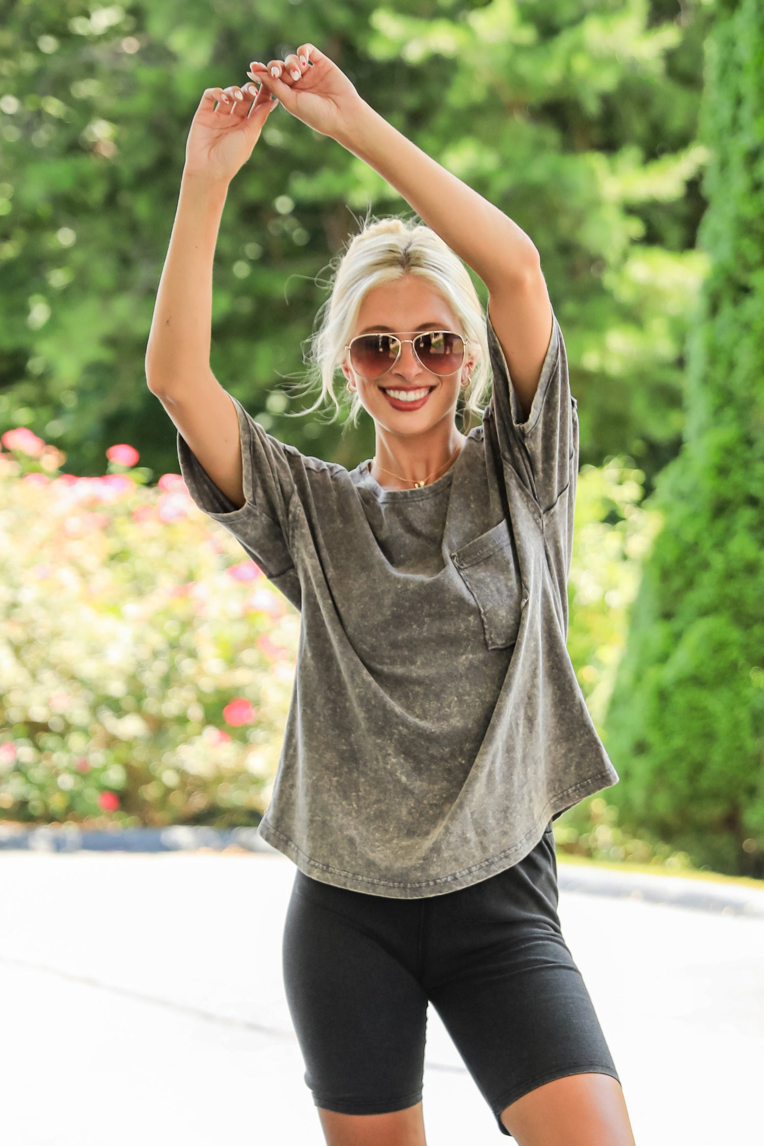 Woman stretching outdoors with sunglasses on, surrounded by greenery and flowers.