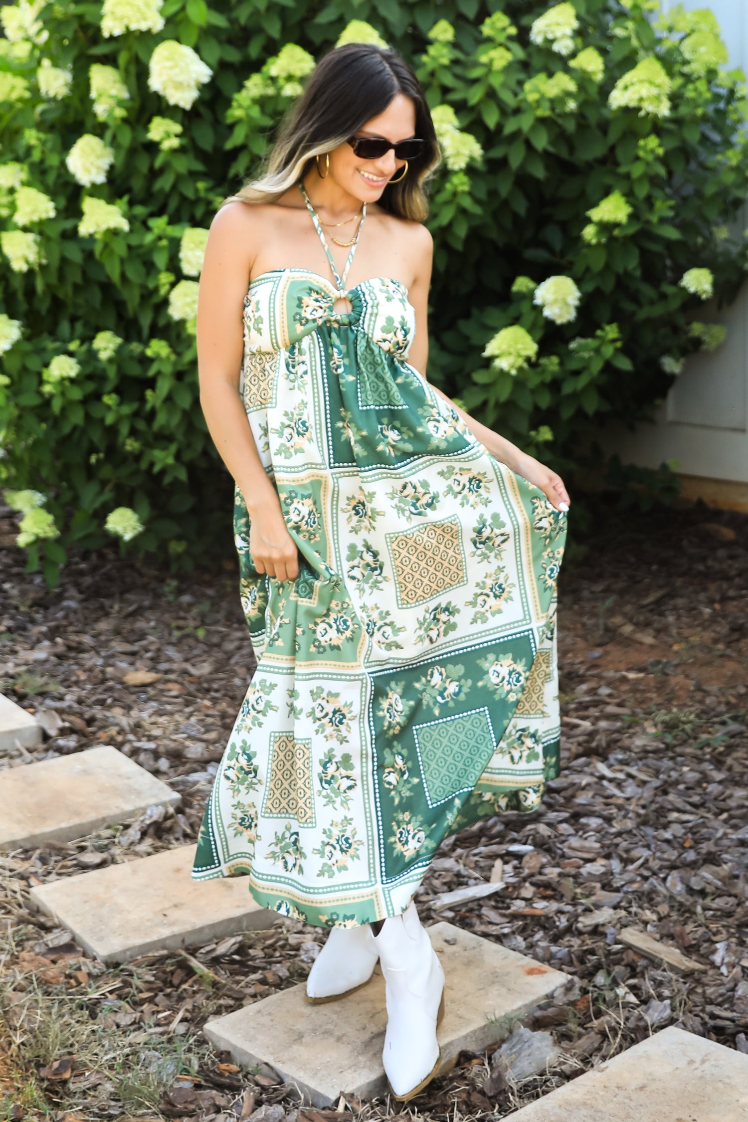 Woman in a green floral dress standing on stone steps with greenery in the background