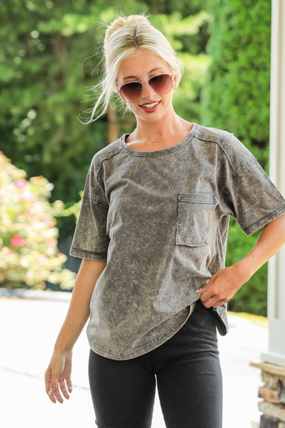 Woman wearing a gray t-shirt and black shorts outdoors with greenery in the background