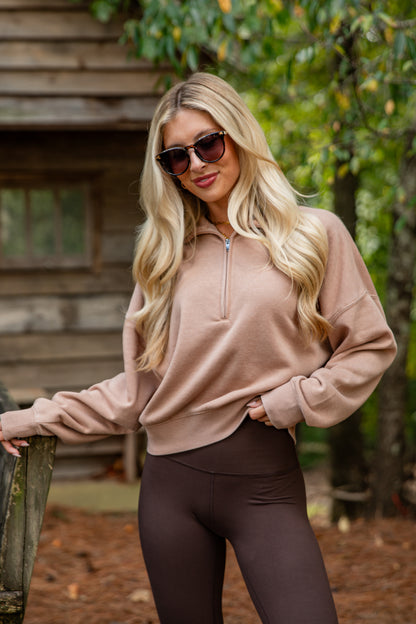Woman wearing a beige hoodie and brown leggings outdoors.