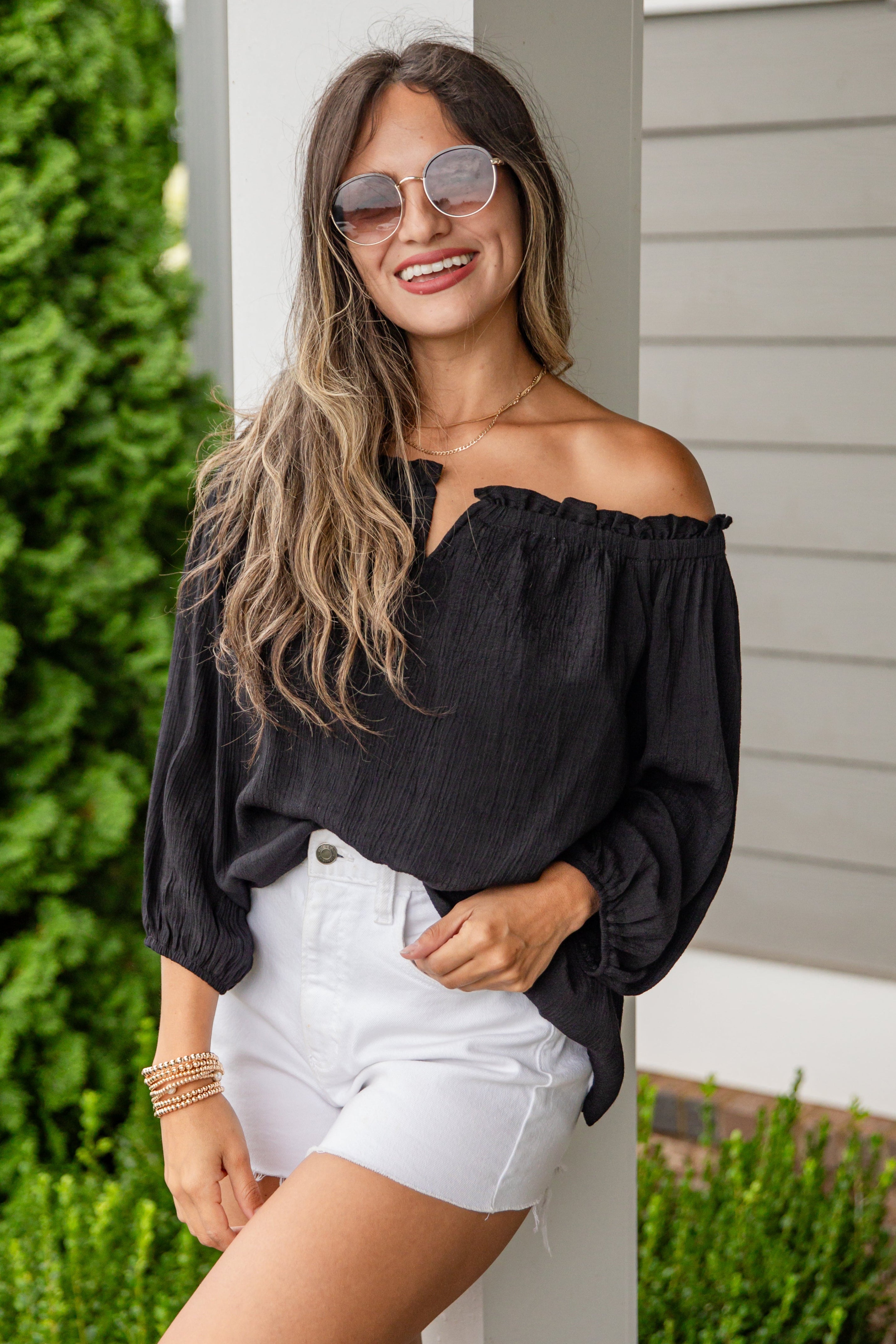 Woman wearing a black off-shoulder top and white shorts standing outdoors.