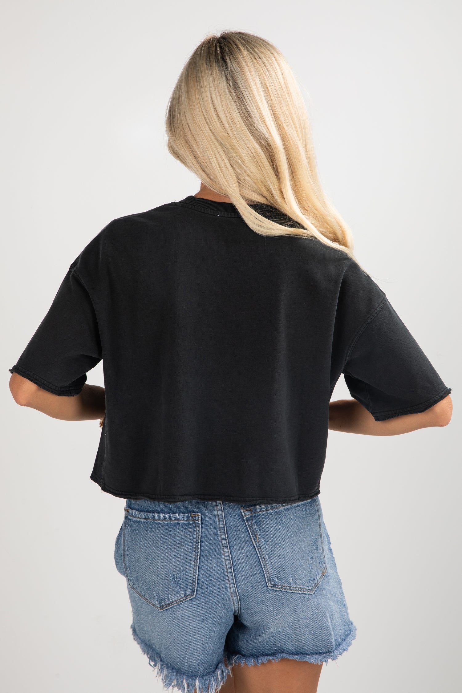 Person wearing a black t-shirt and denim shorts on a plain background