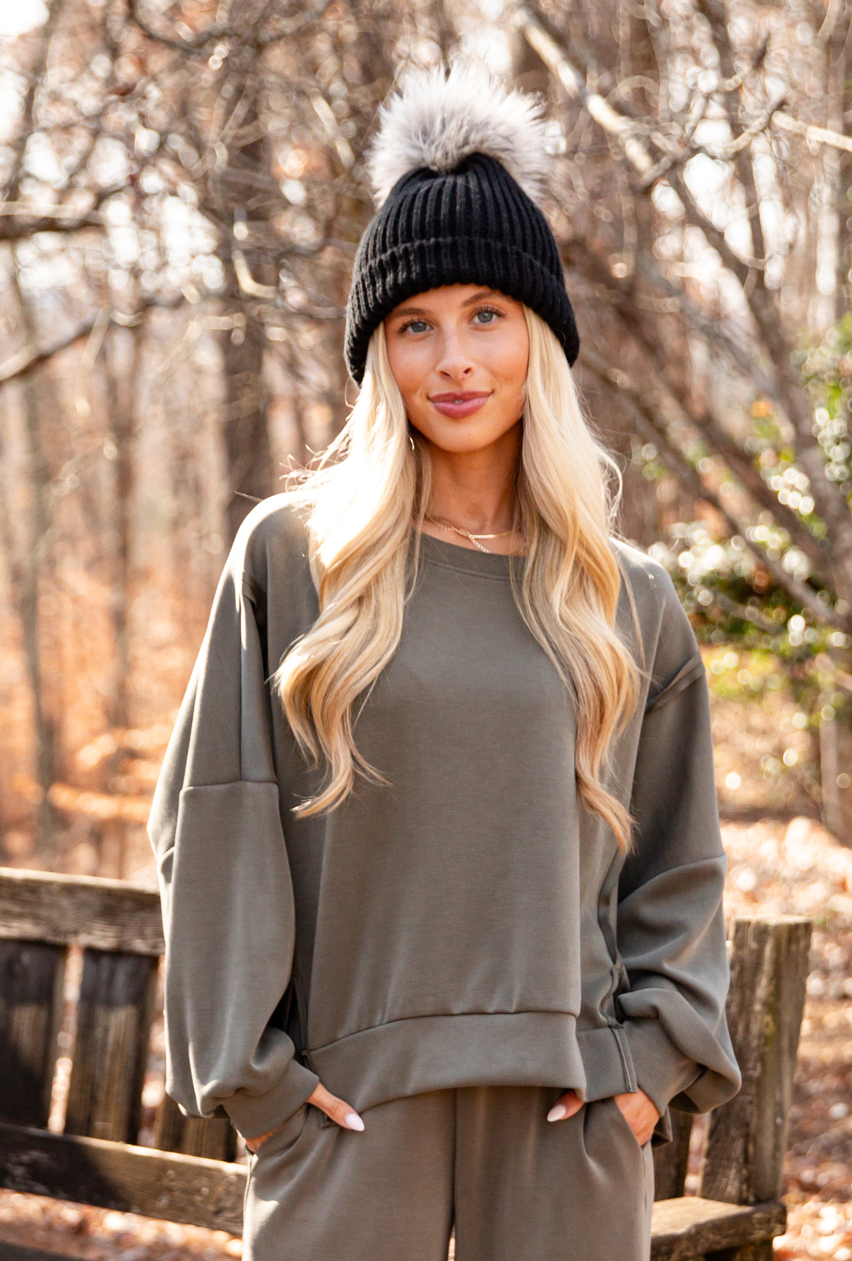 Woman wearing a black beanie and gray sweatshirt in a forest setting