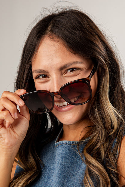 Woman holding sunglasses up to her face with a neutral background