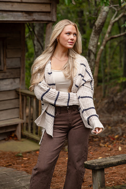 Woman wearing a striped cardigan and brown pants in a forest setting