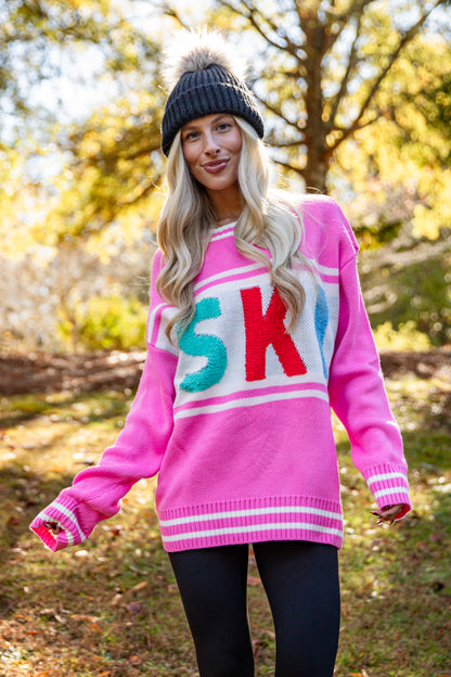 Person wearing a pink sweater with colorful letters outdoors