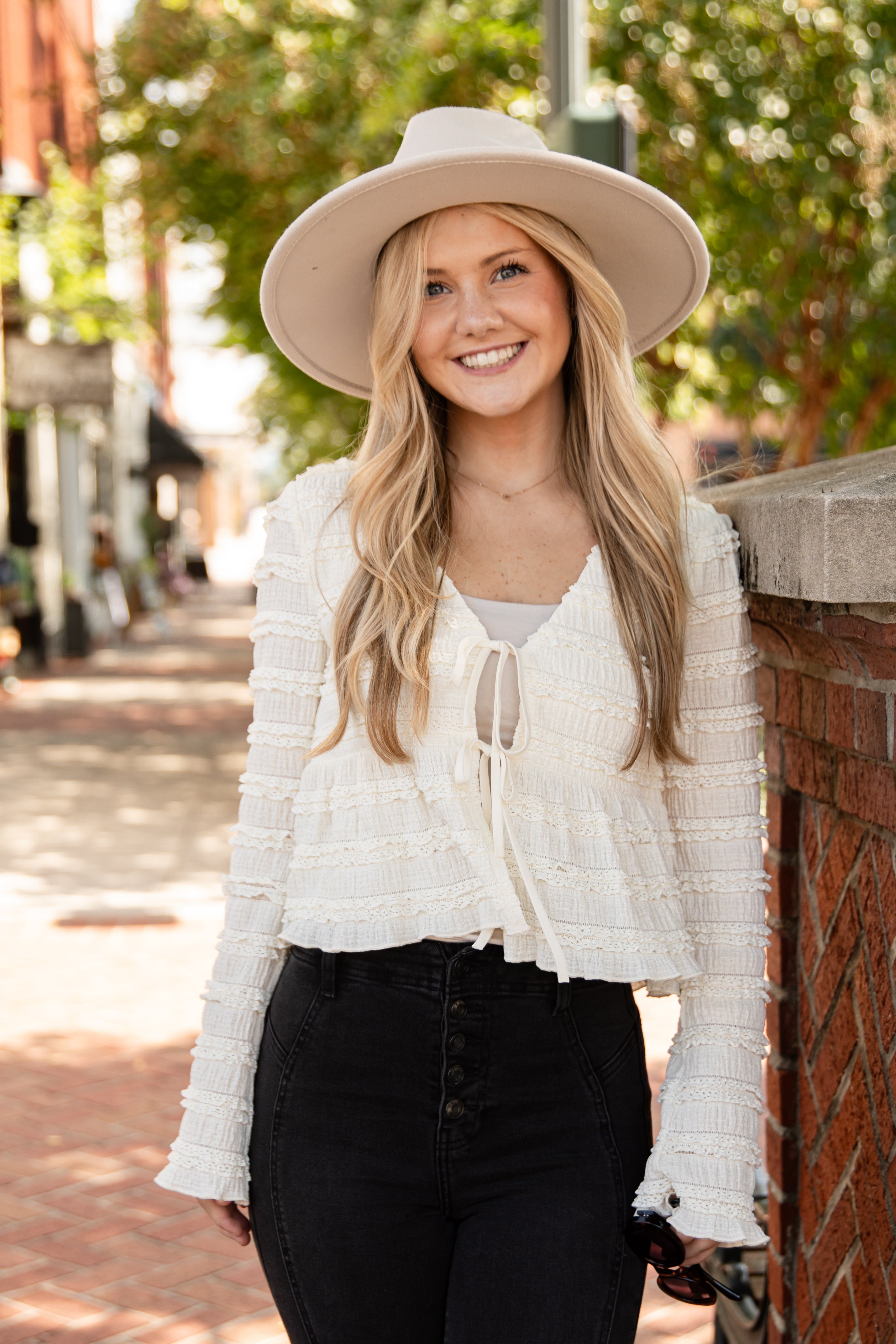 Woman wearing a white top, black pants, and a beige hat on a street.