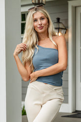 Woman standing on a porch wearing a blue top and white pants.