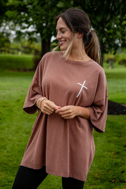 Woman wearing a brown oversized t-shirt with a white cross design outdoors.