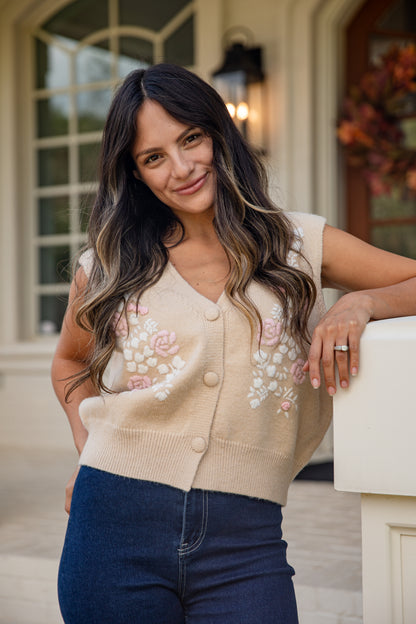 Woman wearing a beige cardigan with floral embroidery standing outdoors.