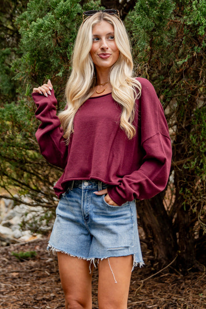 Woman wearing a maroon sweater and denim shorts standing in a natural setting.