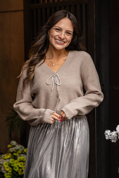 Woman wearing a beige sweater and silver skirt standing in front of a decorative door with flowers.