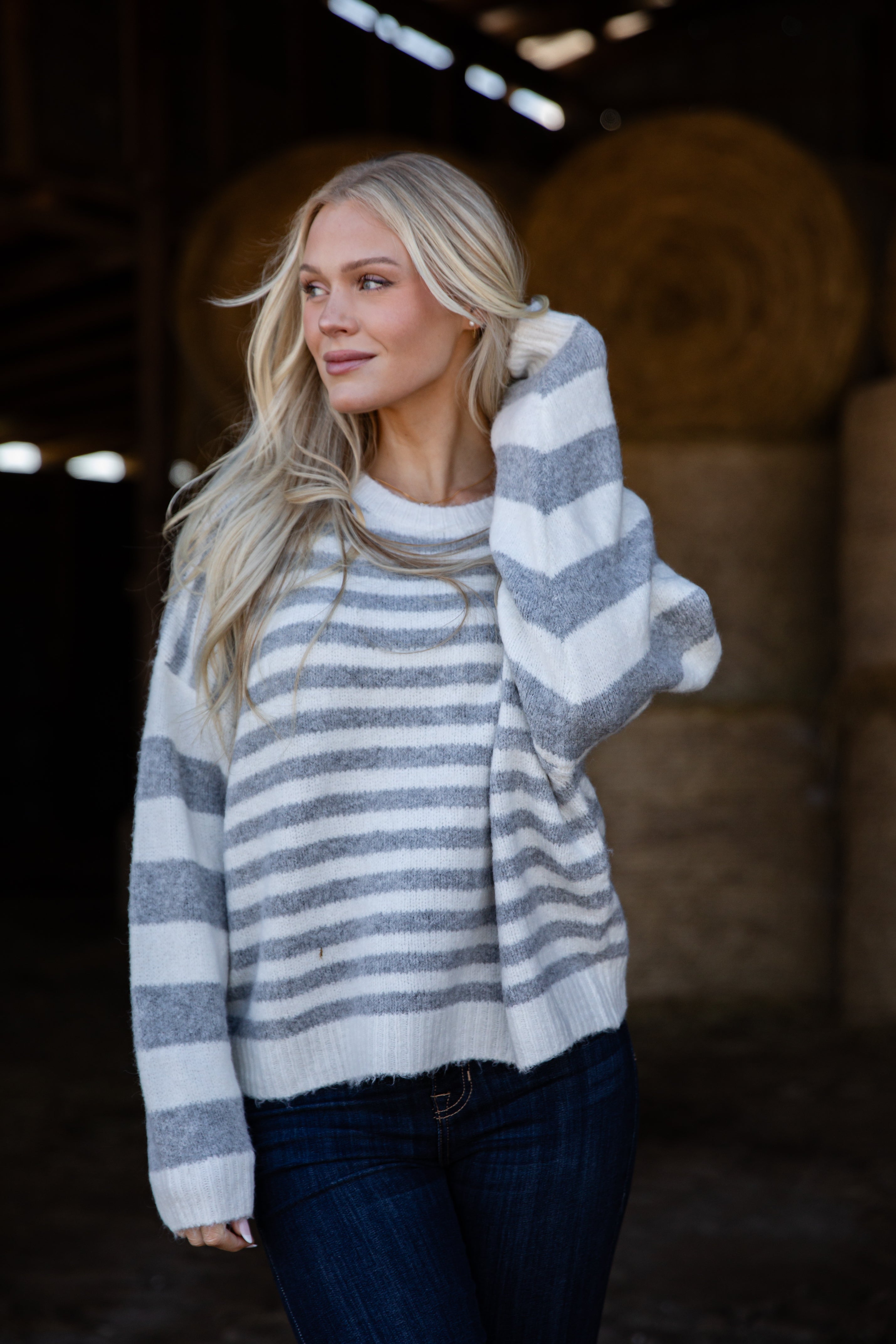 Woman wearing a gray and white striped sweater in a dimly lit indoor setting.