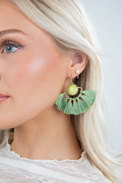 Close-up of a woman wearing green tassel earrings with a light background