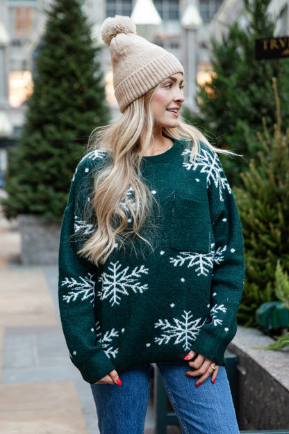 Woman wearing a green sweater with snowflake patterns and a beige beanie outdoors.