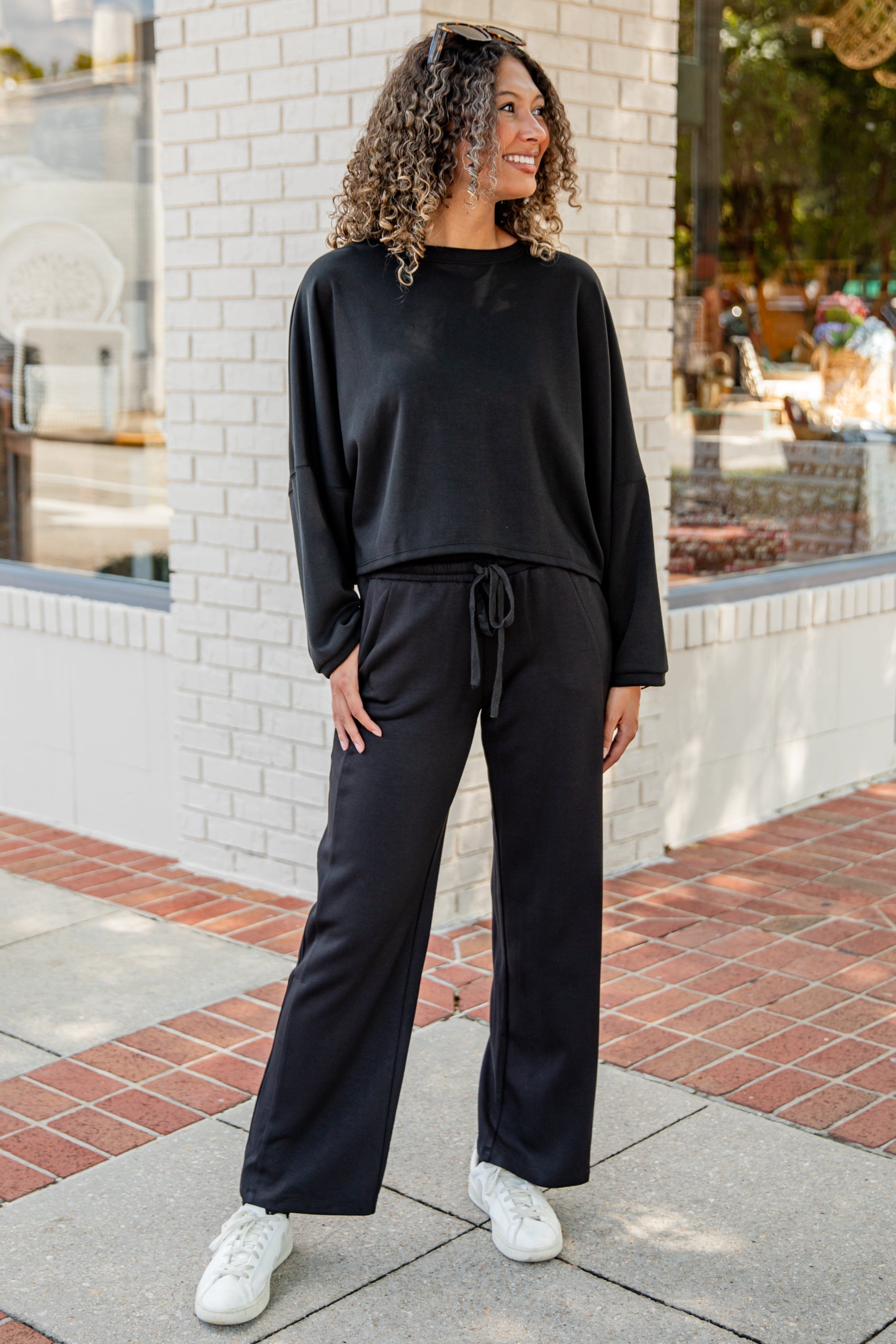 Woman wearing a black outfit standing on a sidewalk with a building in the background
