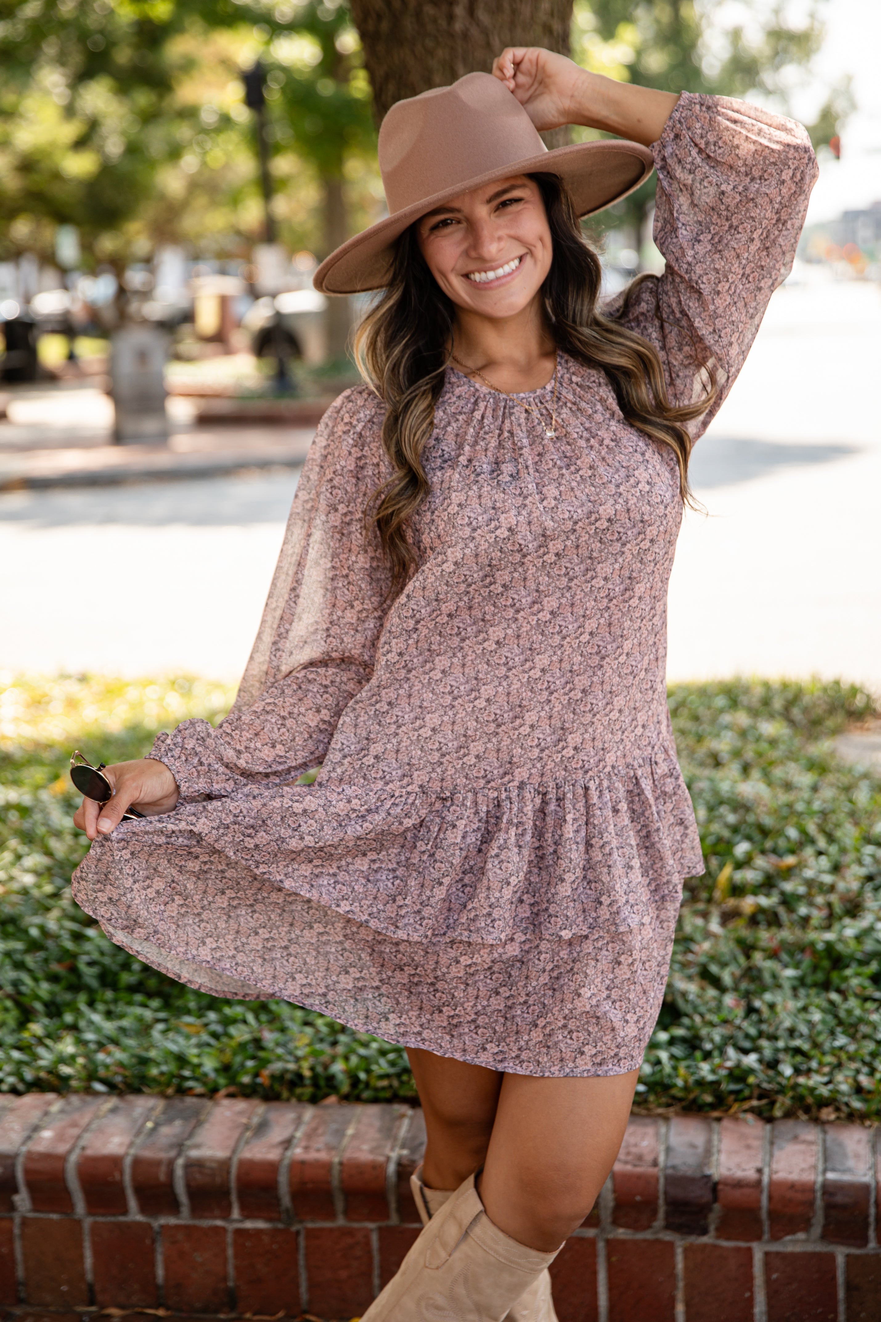 Woman in a floral dress and wide-brimmed hat standing outdoors.