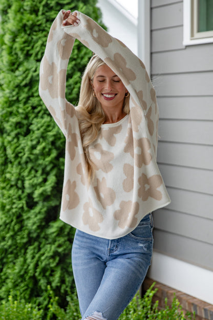 Woman in a patterned top and jeans standing on a wooden deck with greenery and a house in the background.