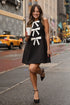 Woman in a black dress with white bow design walking on a city street.
