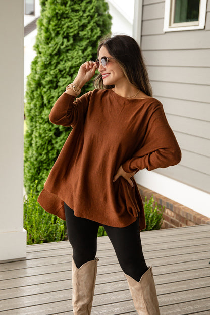 Woman wearing a brown sweater and beige boots on a wooden deck.
