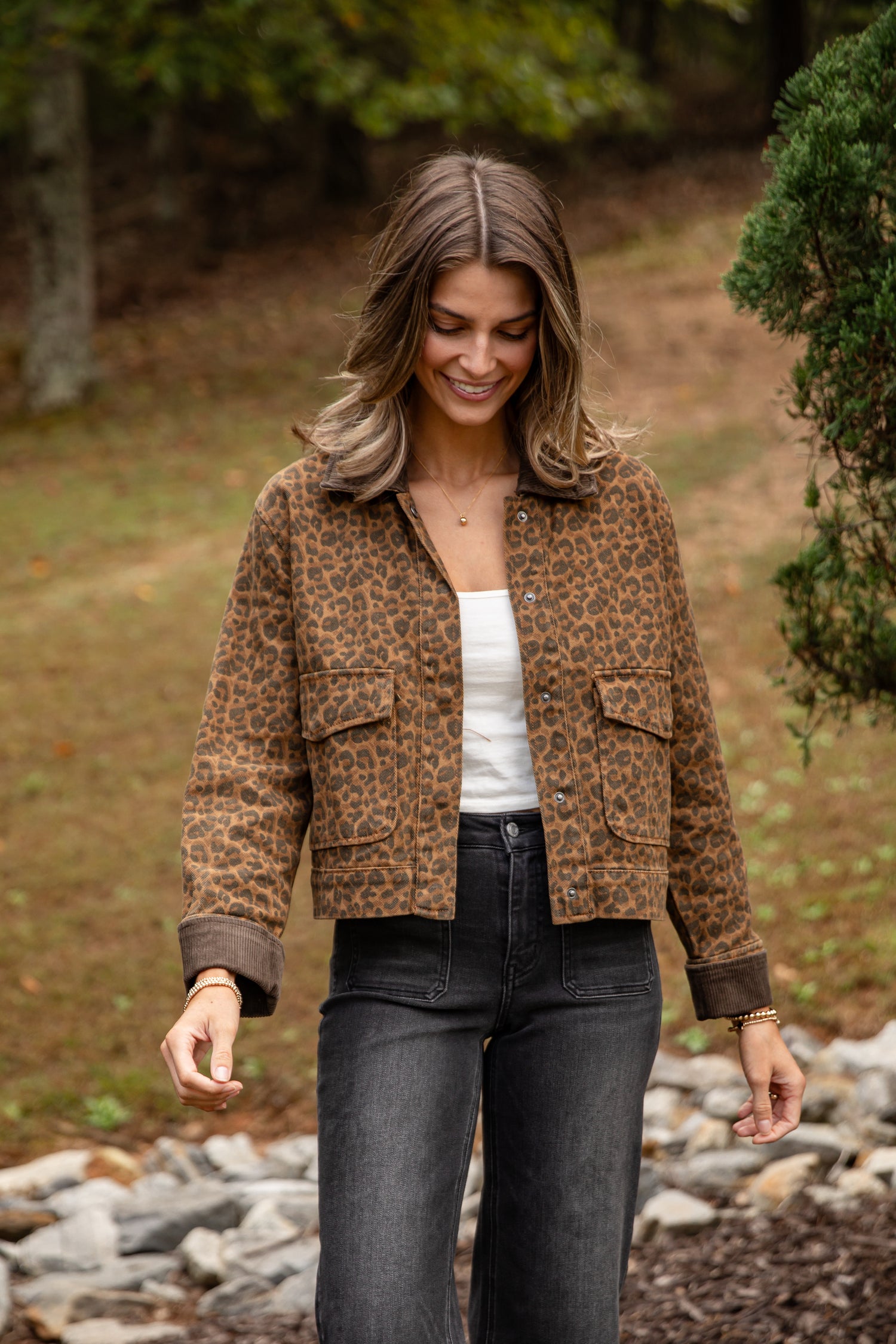 Woman wearing a leopard print jacket in a natural setting with trees and rocks.