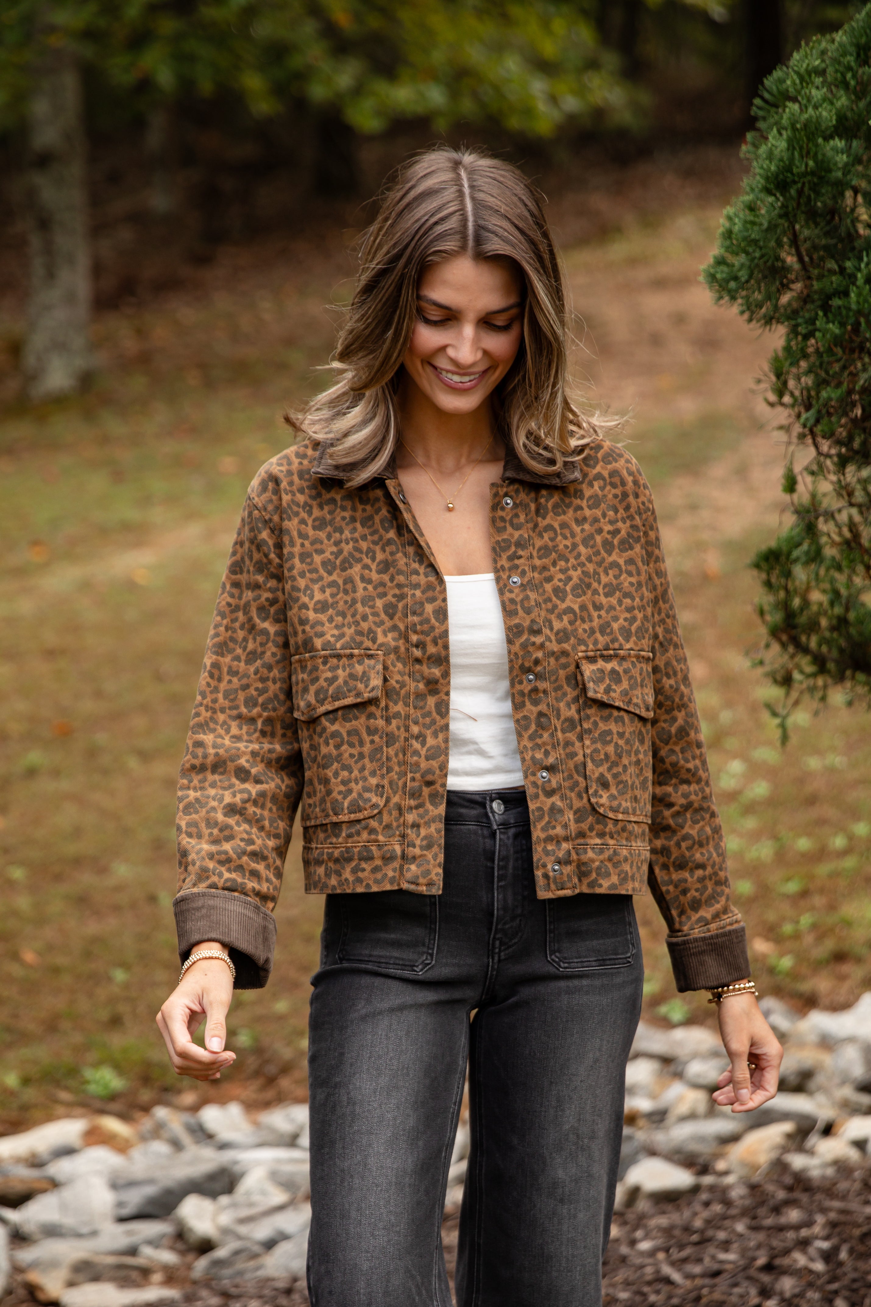 Woman wearing a leopard print jacket in a natural setting with trees and rocks.