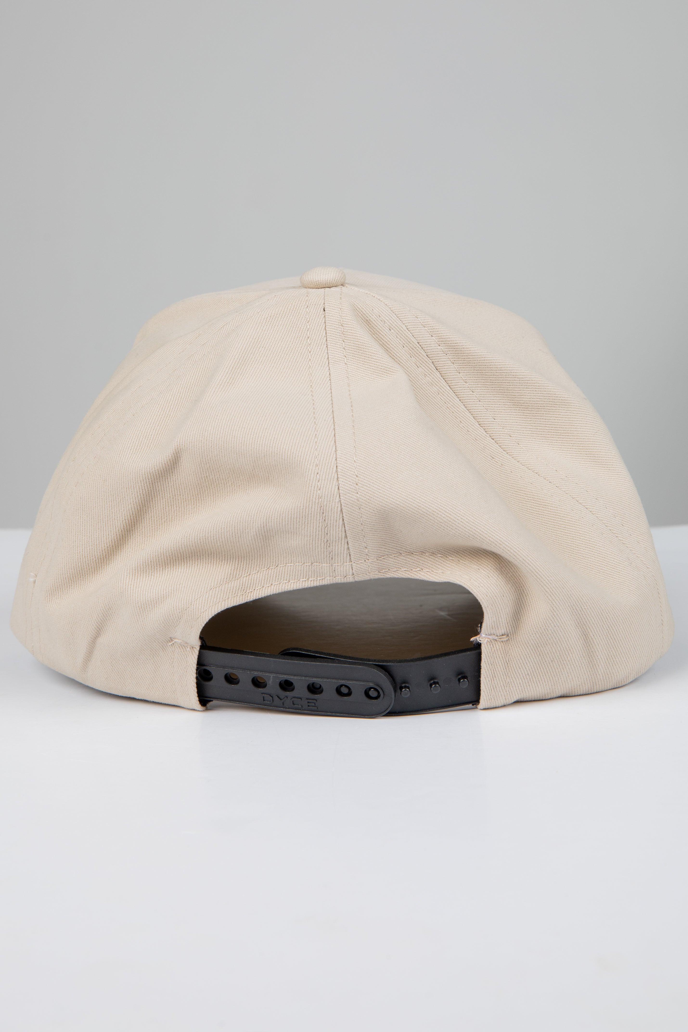 Beige cap with a black adjustable strap on a light gray background