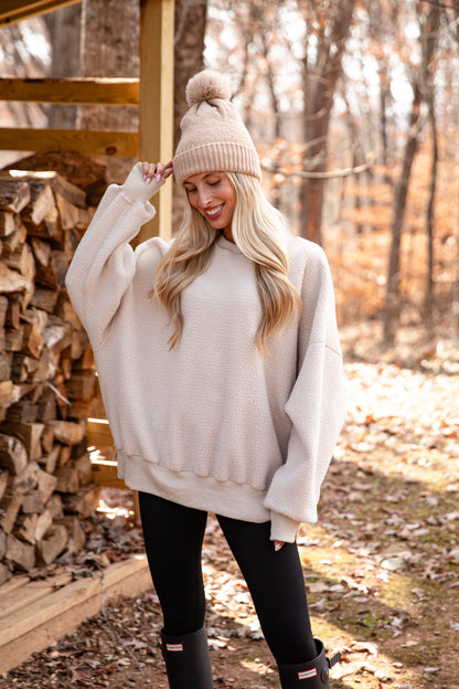 Woman wearing a beige sweater, black leggings, and a pink beanie in a forest setting.