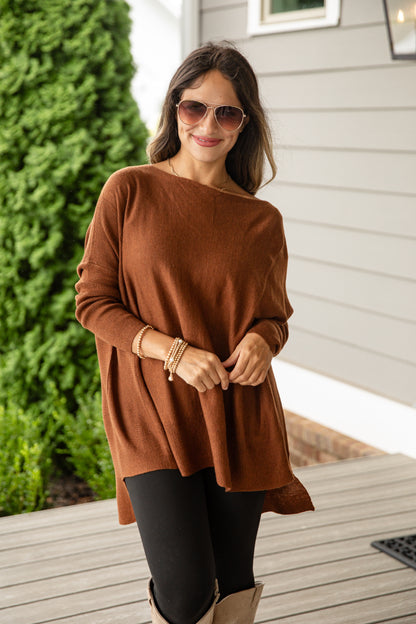 Woman wearing a brown sweater and black leggings outdoors on a wooden deck.