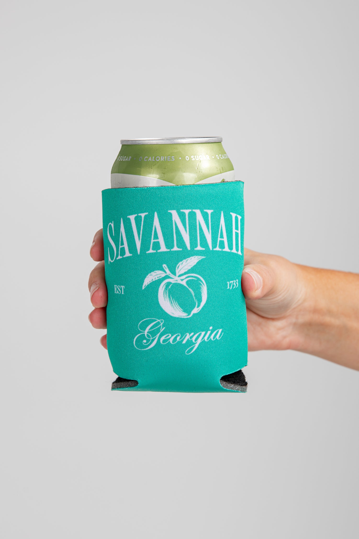 Hand holding a can with a teal sleeve featuring &