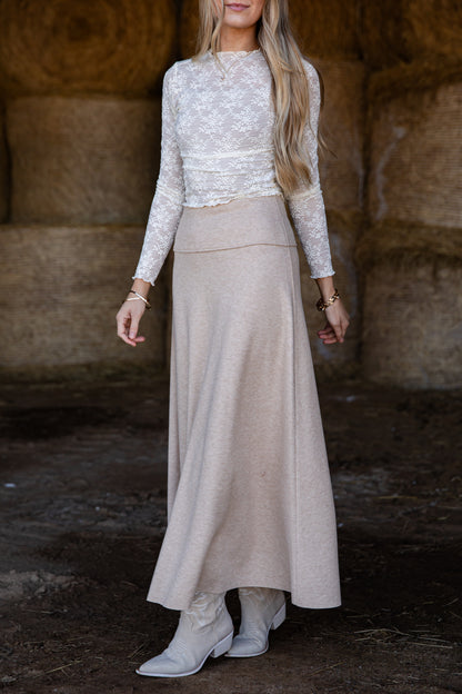 Woman wearing a white lace top and beige skirt in a rustic setting