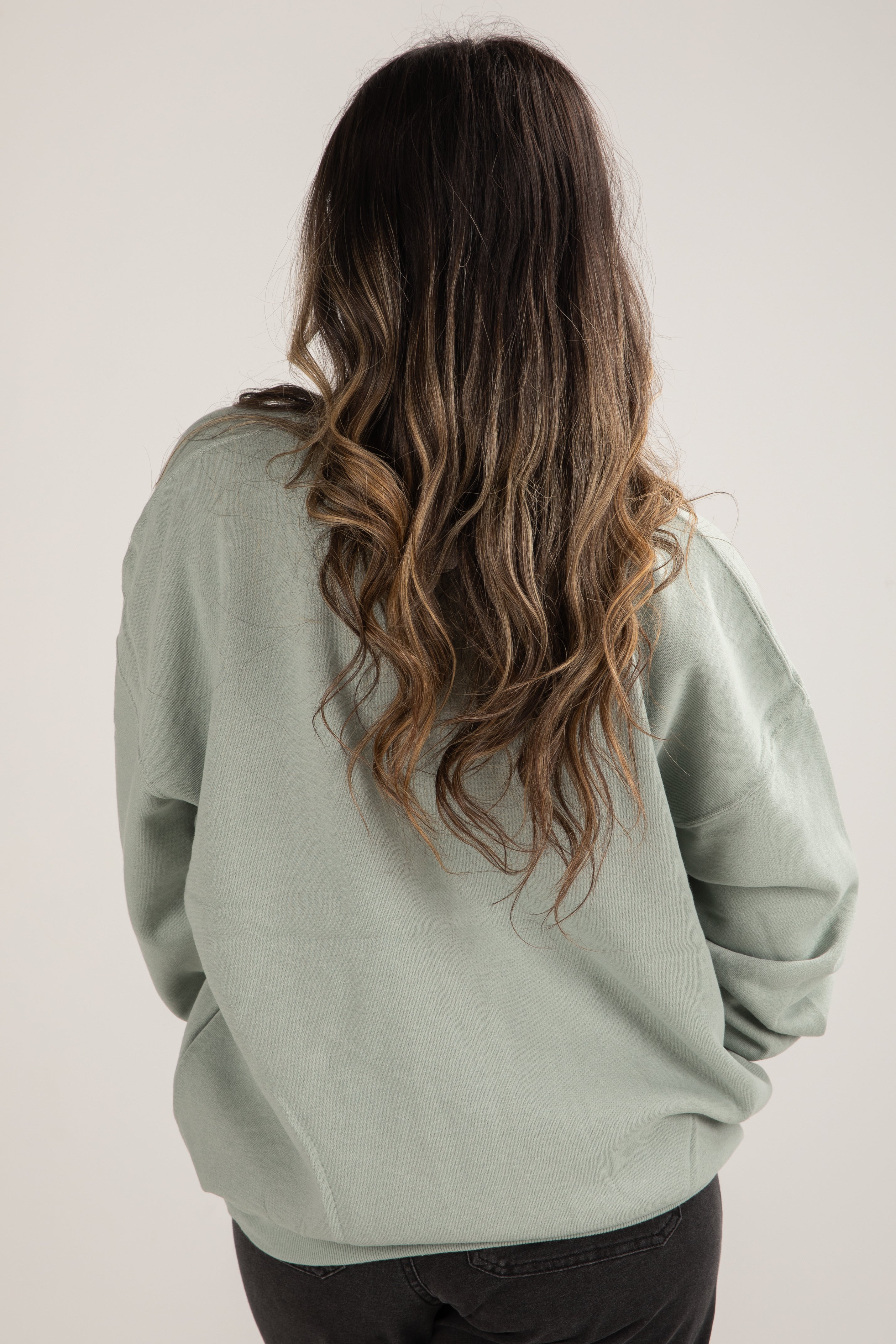 Person wearing a light green sweatshirt with long, wavy hair on a plain background