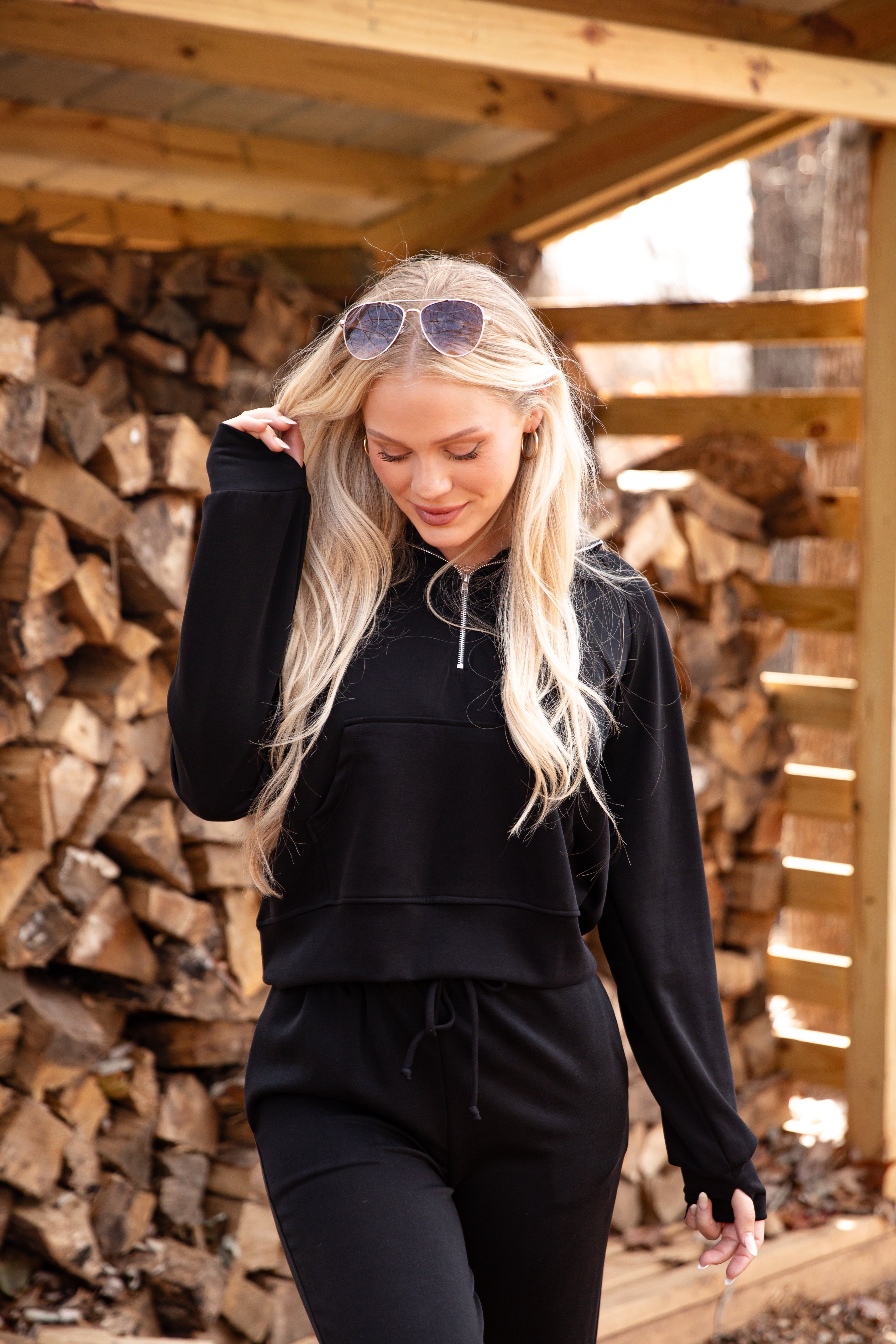 Woman in black hoodie and pants standing in front of stacked firewood