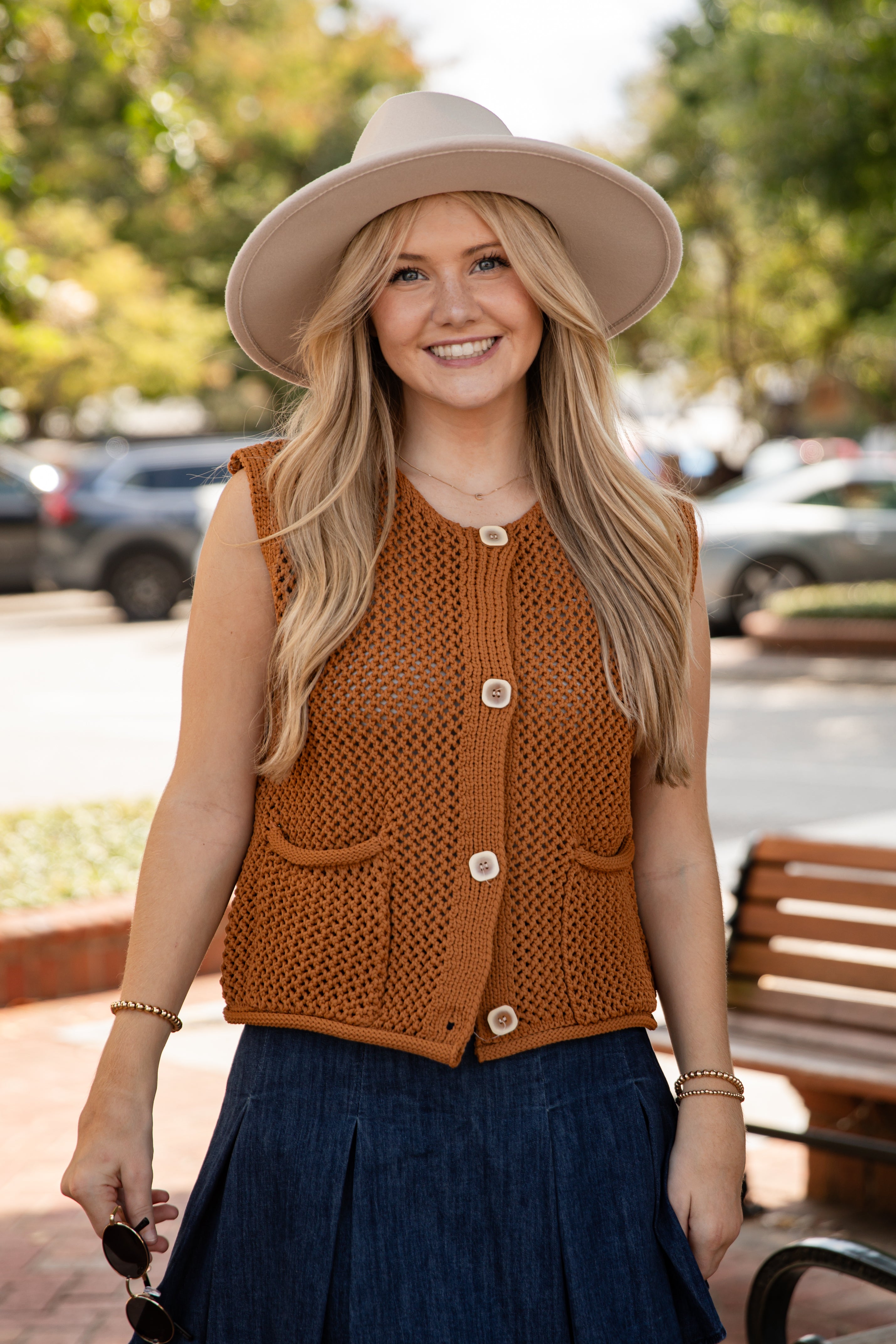 Woman wearing a brown vest and beige hat outdoors