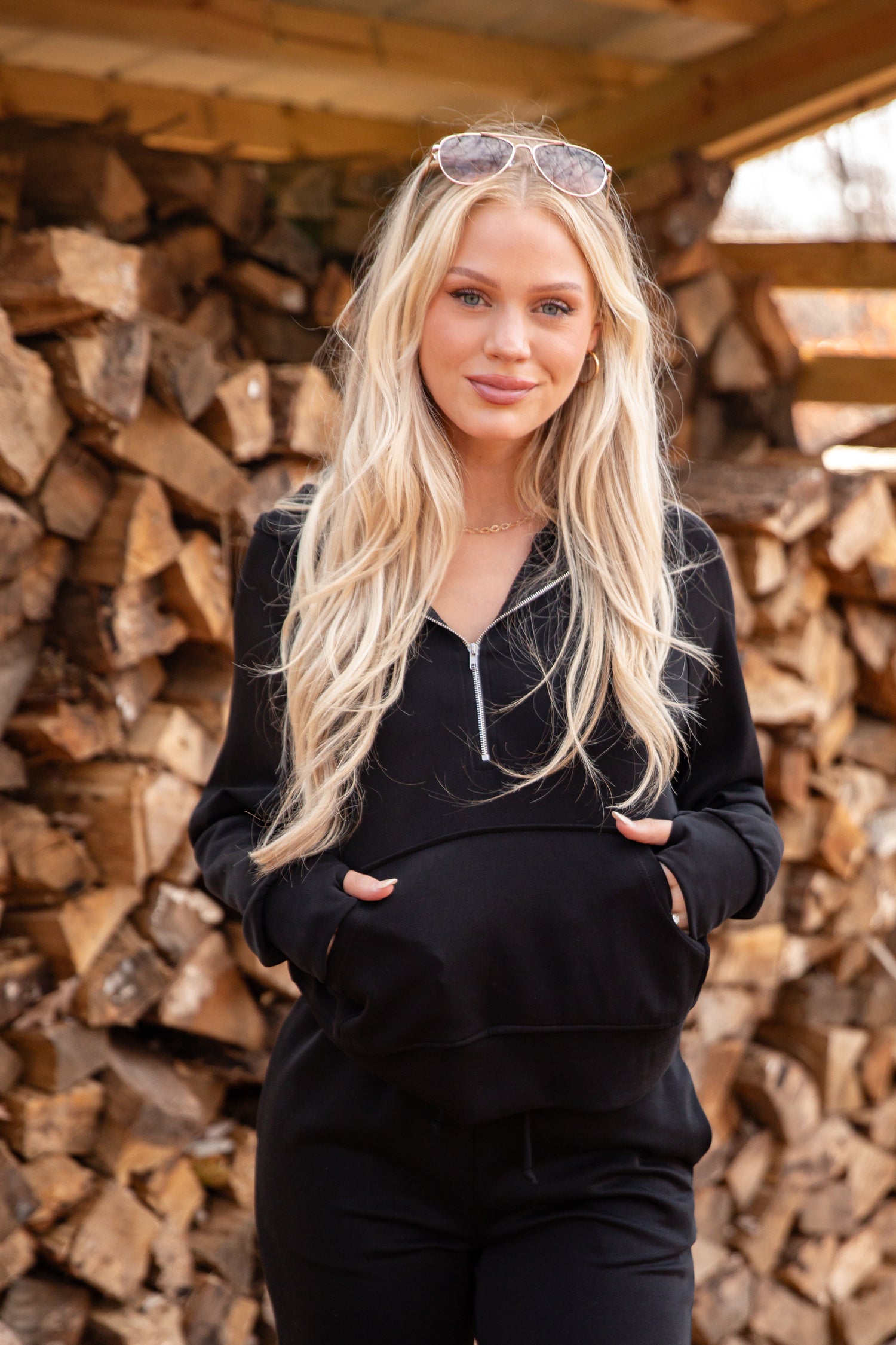 Woman in black outfit standing in front of stacked firewood