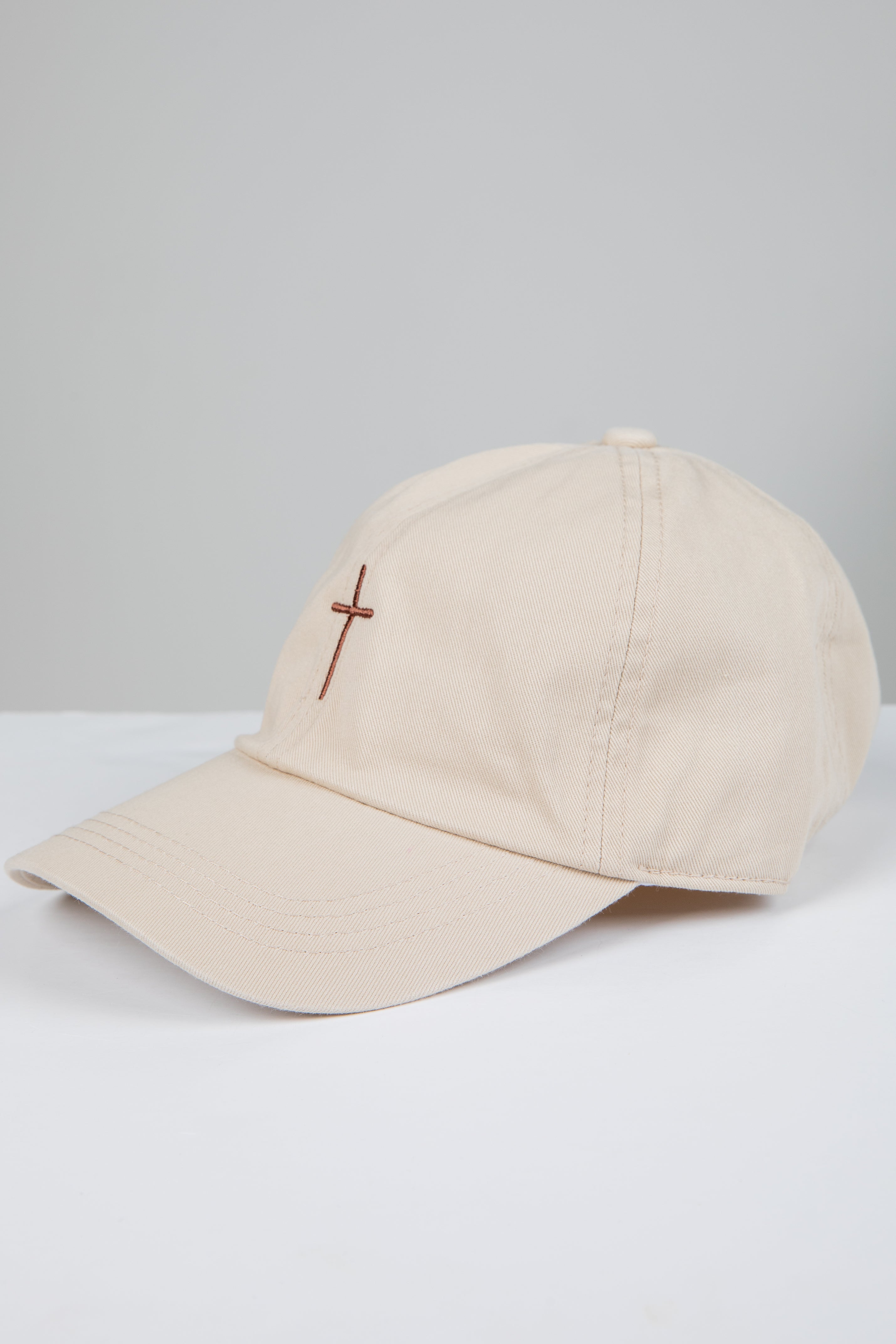 Beige cap with a cross emblem on a light gray background
