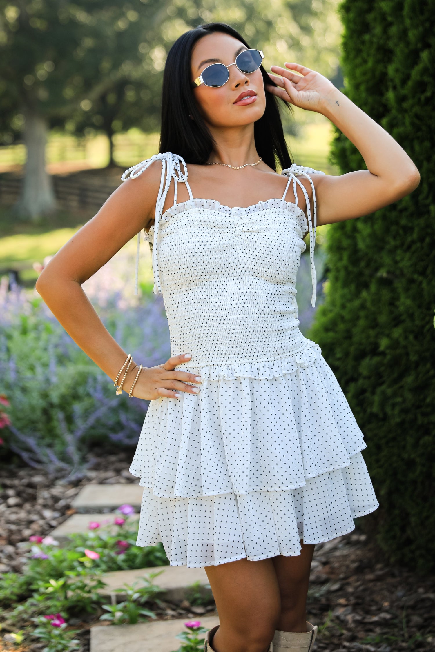 Woman in a white dress standing outdoors with greenery and flowers in the background