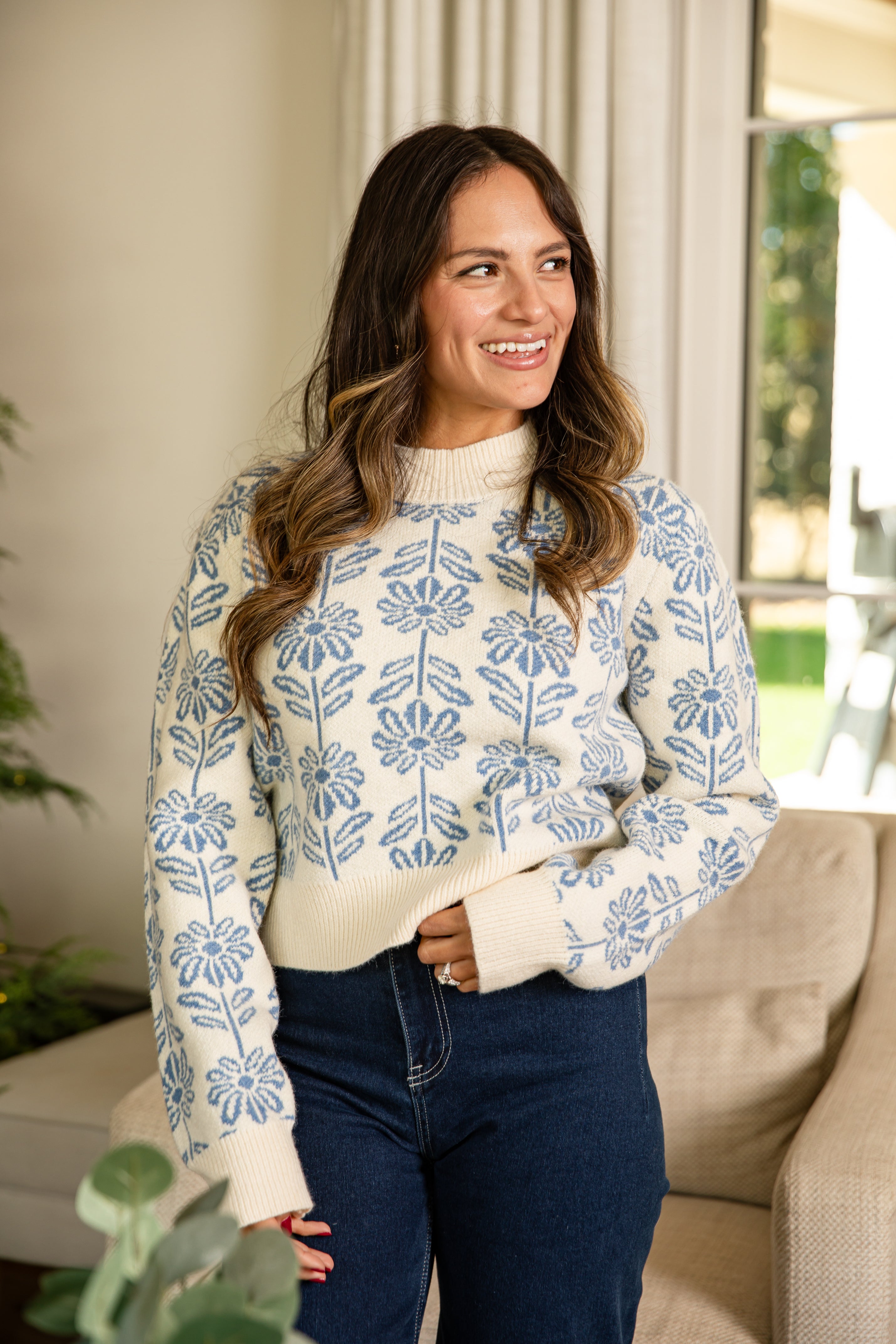 Woman wearing a white sweater with blue floral pattern indoors