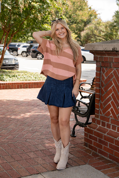 Woman in a striped shirt and skirt standing on a sidewalk with cars and trees in the background