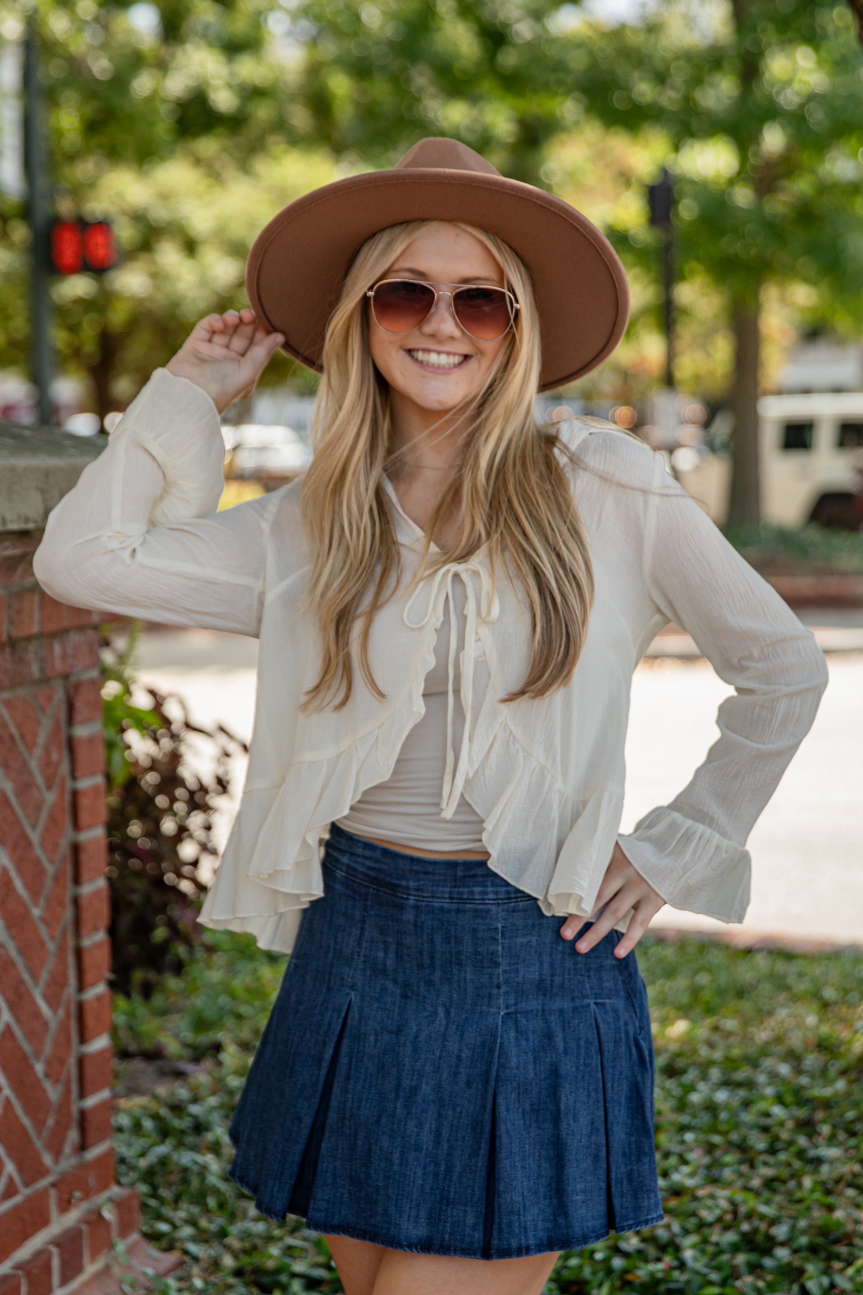 Woman wearing a white blouse, blue skirt, and brown hat outdoors.